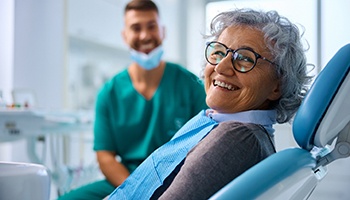 Woman with black glasses smiling while sitting in treatment chair