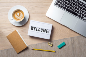 A note that says “welcome” next to a cup of coffee and a laptop